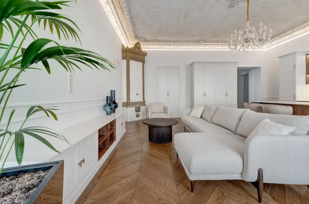 Elegancki salon z sofą i stolikiem kawowym, ozdobiony sztukaterią i żyrandolem. Podłoga w stylu jodełka francuska dodaje wnętrzu klasy.