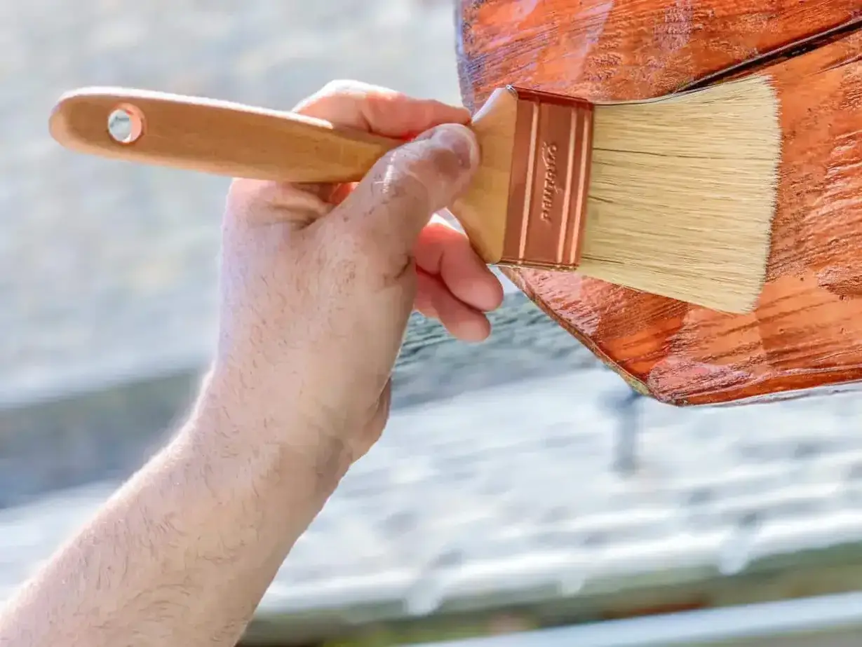 Mano aplicando barniz a una mesa de madera exterior. El proceso de pintar mesa de madera exterior para protegerla.