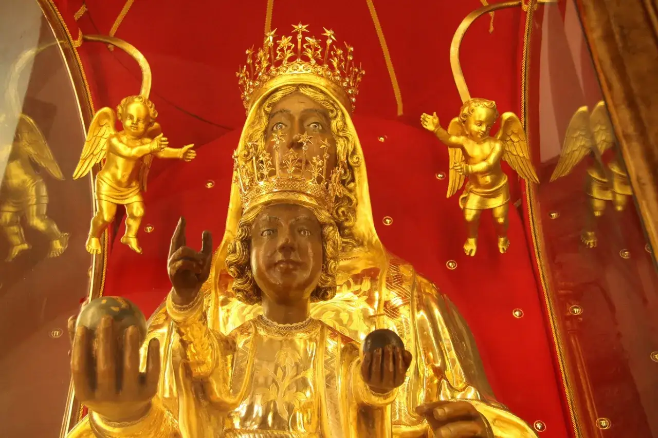 Statua dorata della Madonna Nera con Bambino, circondata da angeli dorati. Il suo aspetto misterioso evoca il madonna nera significato esoterico.