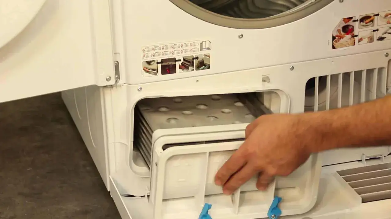 Main d'homme retirant le filtre d'un s&egrave;che-linge qui ne s&egrave;che plus. Le filtre est plein de peluches.