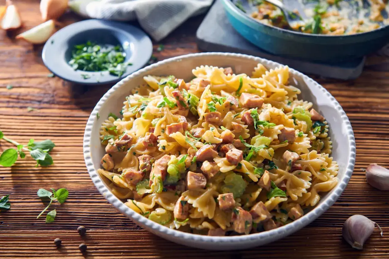 Pyszny makaron farfalle z kawałkami kiełbasy i zieloną pietruszką, podany w białej misce na drewnianym stole.
