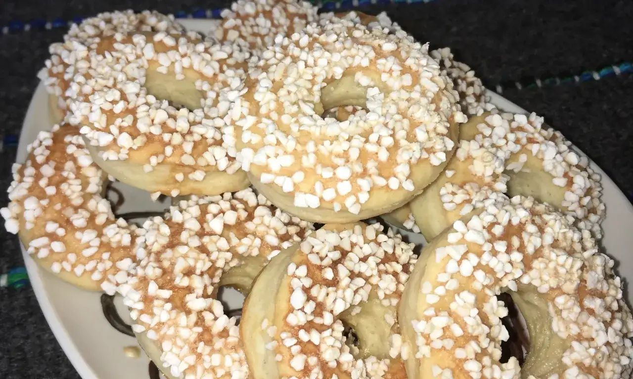 En hög med gyllene finska pinnar, strösslade med sockerpärlor, ligger på en vit tallrik.