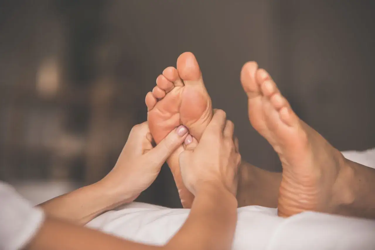 Hands giving soothing foot massages to a person lying on a white surface.