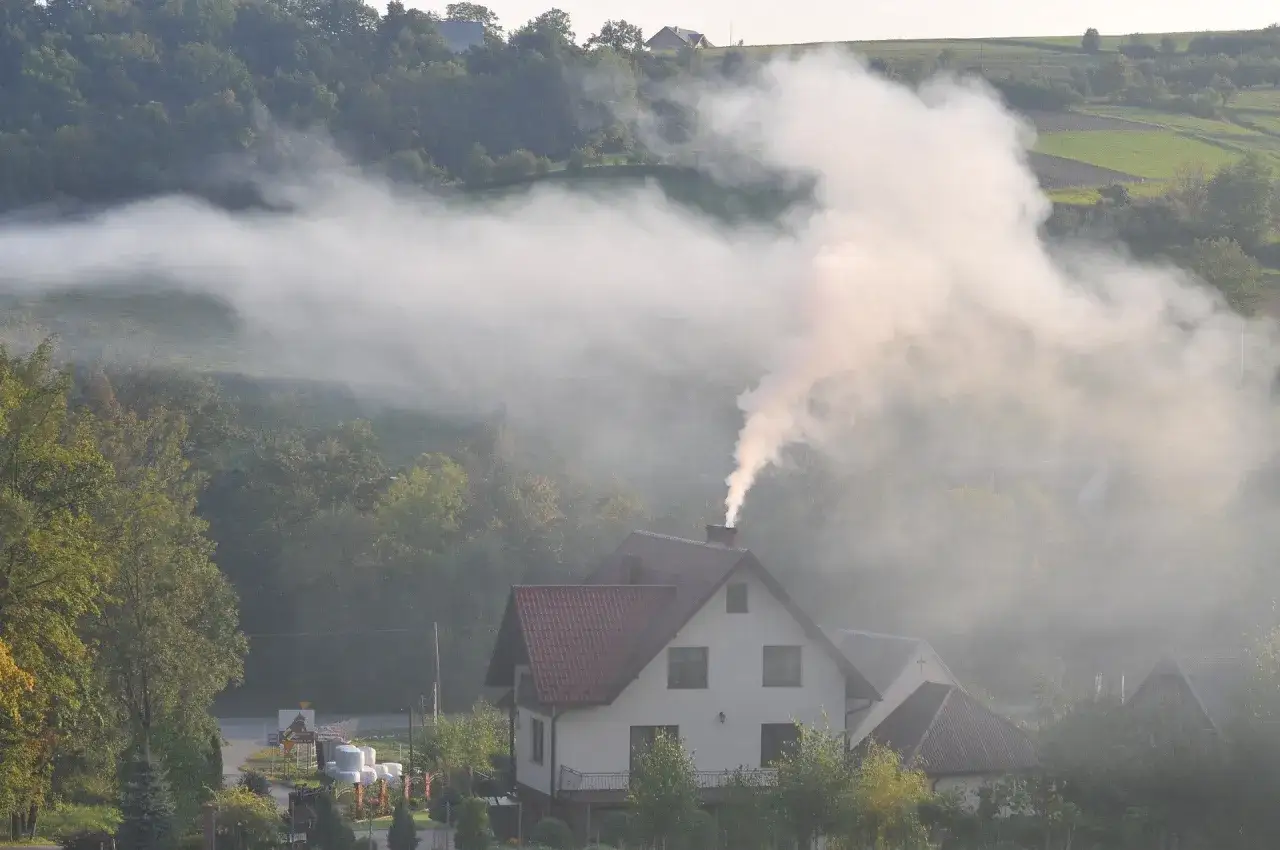 Dym z komina domu w dolinie. Jak zapobiegać smogowi? Brainly podpowiada: czyste ogrzewanie.