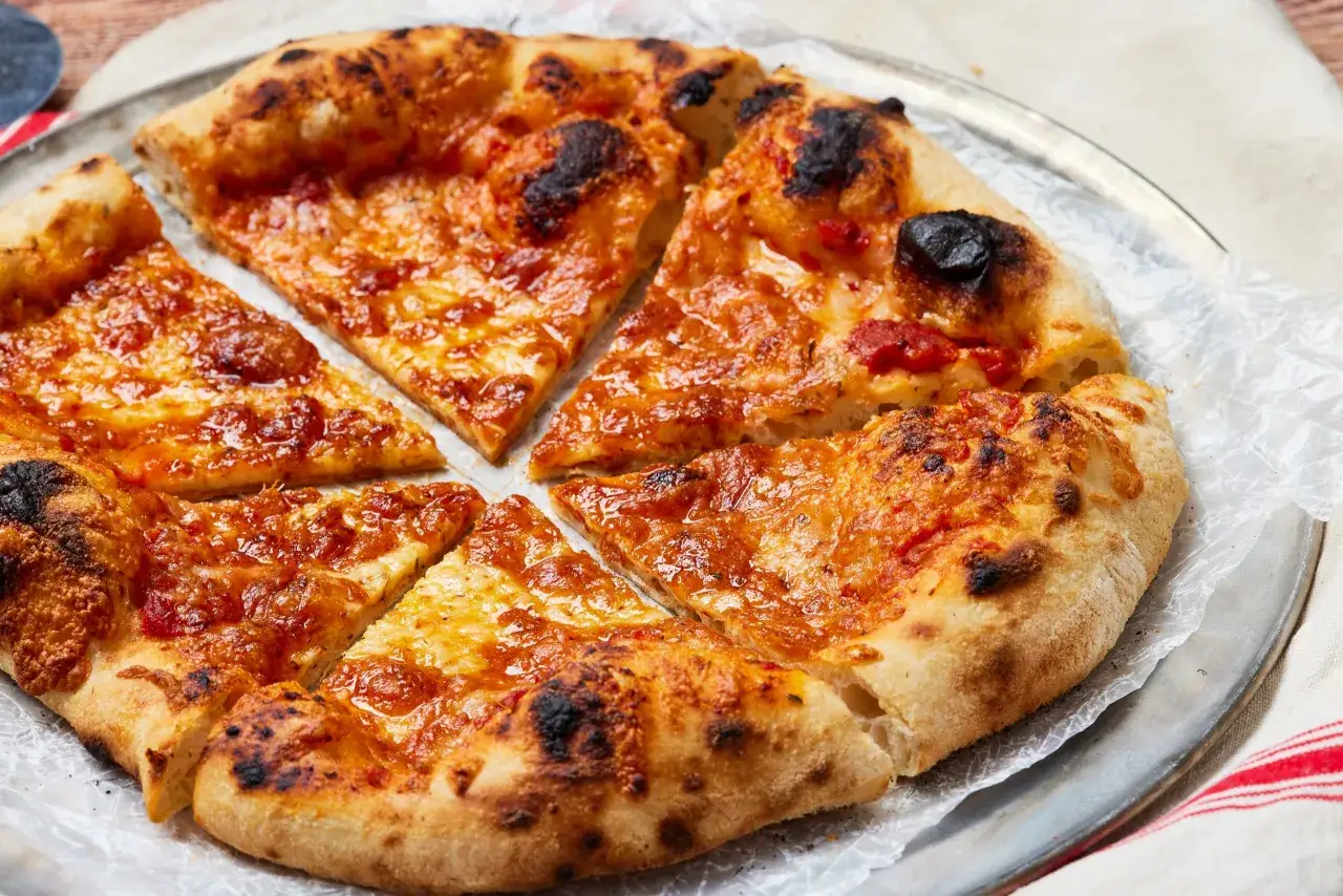 Pyszna, pokrojona pizza z ciągnącym serem i lekko przypalonymi brzegami. Idealne składniki na pizzę do szybkiego obiadu.