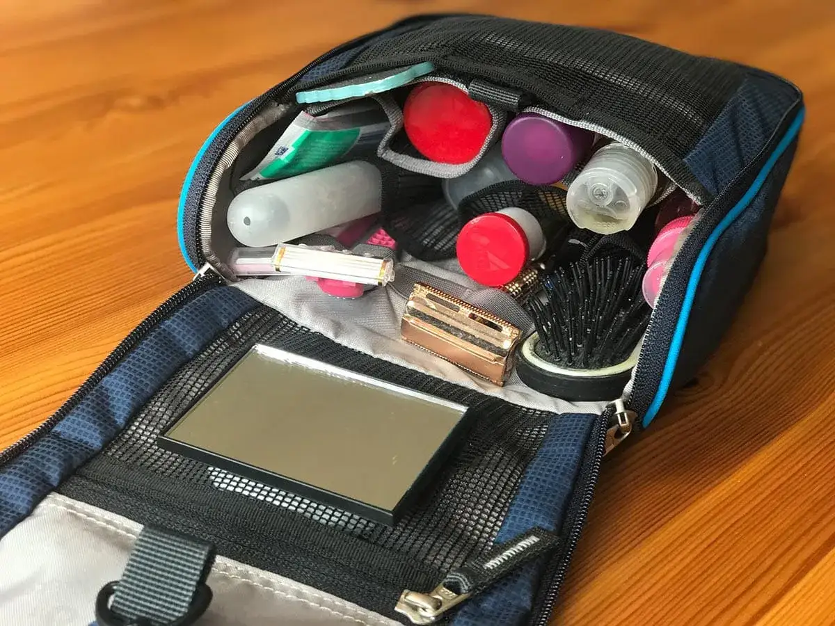 Offener Kulturbeutel mit vielen Pflegeprodukten: Zahnbürste, Rasierer, Spiegel, Bürste und diverse Fläschchen. Perfekte Packliste für die Reise.