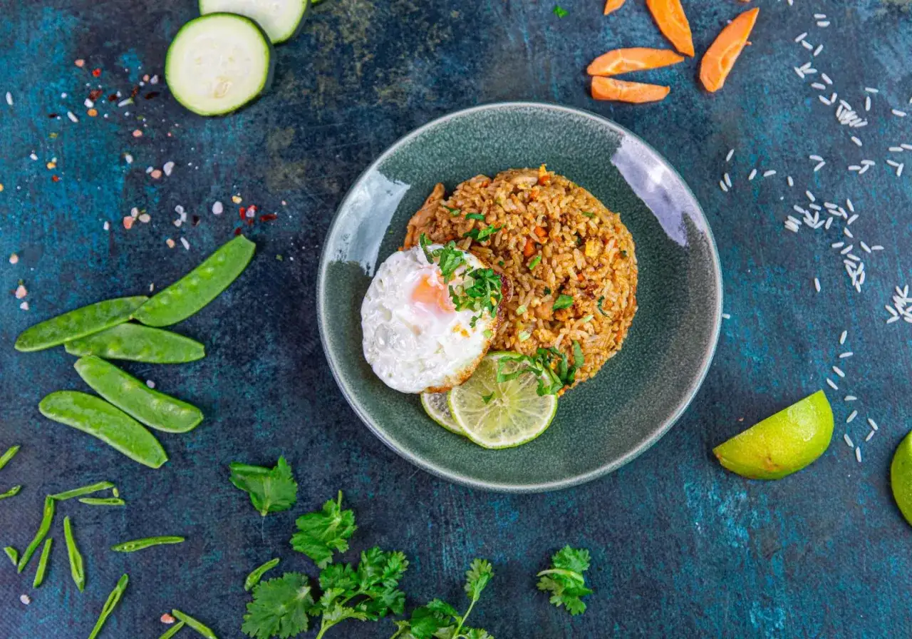 Nasi goreng z jajkiem sadzonym i limonką, otoczony groszkiem cukrowym, marchewką i świeżą kolendrą.