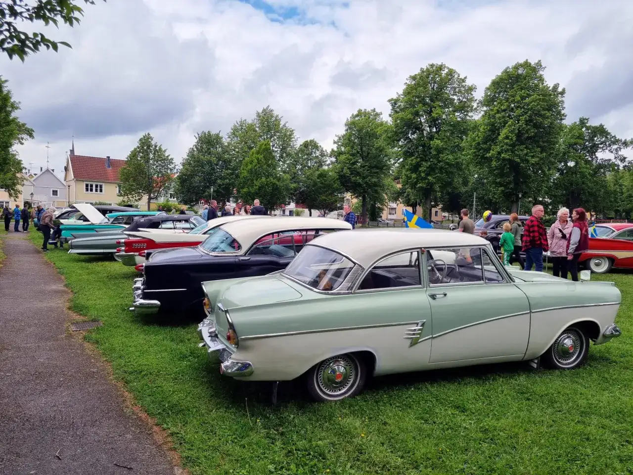 En samling gamla bilmodeller st&aring;r uppradade p&aring; en gr&auml;smatta. M&auml;nniskor beundrar de klassiska fordonen under en molnig himmel.