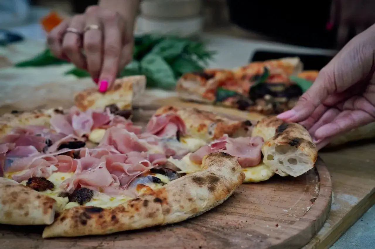 Zwei H&auml;nde greifen nach verschiedenen Pizza-Sorten. Eine Pizza ist mit Schinken und K&auml;se belegt, die andere mit Gem&uuml;se.