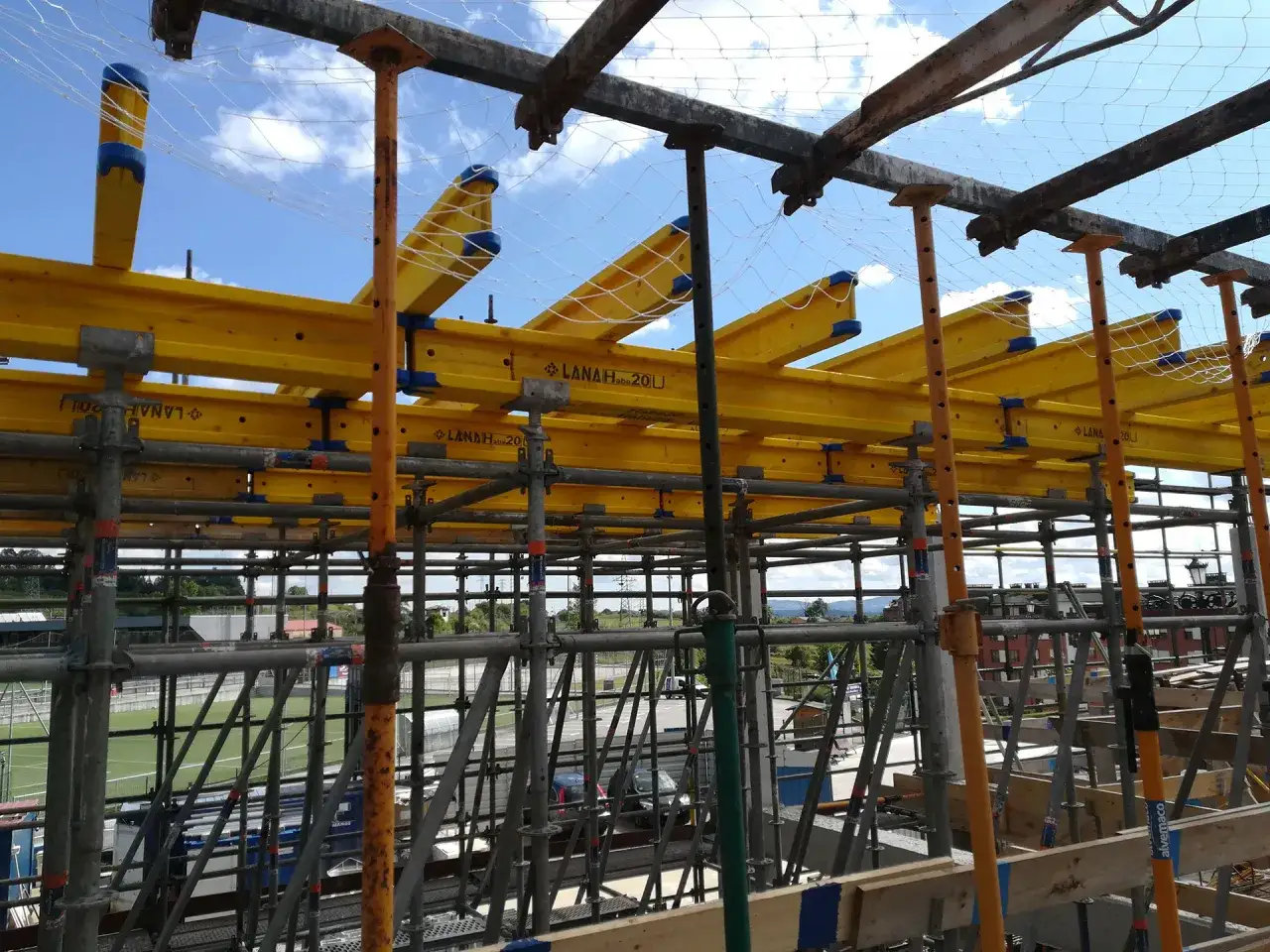 Estructuras temporales amarillas y grises sostienen una red de seguridad bajo un cielo azul.