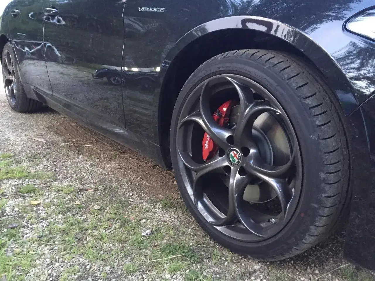 Czarne Alfa Romeo Giulia Veloce z czerwonymi zaciskami hamulcowymi i felgami w kształcie liścia.