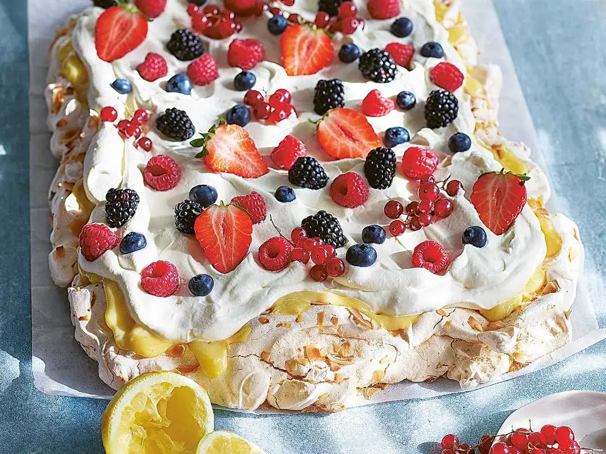 En stor pavlova tårta med vispgrädde, lemon curd och massor av färska bär som jordgubbar, hallon, blåbär och vinbär.