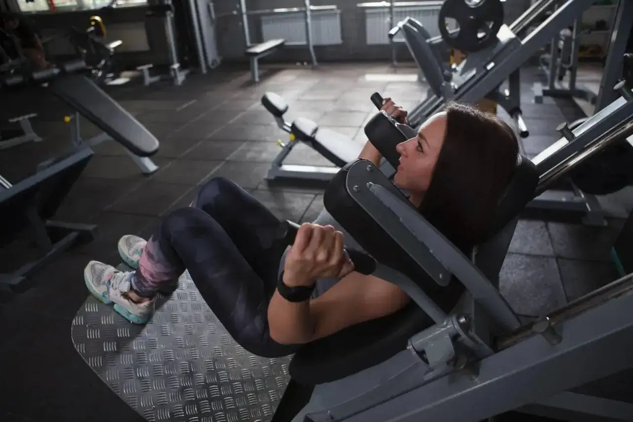 Kvinna tränar ben på en hack squat-maskin i ett gym.