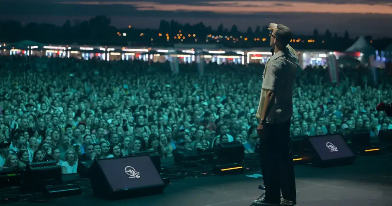 Artysta na scenie, przed tłumem śpiewającym hymny męskiego grania.