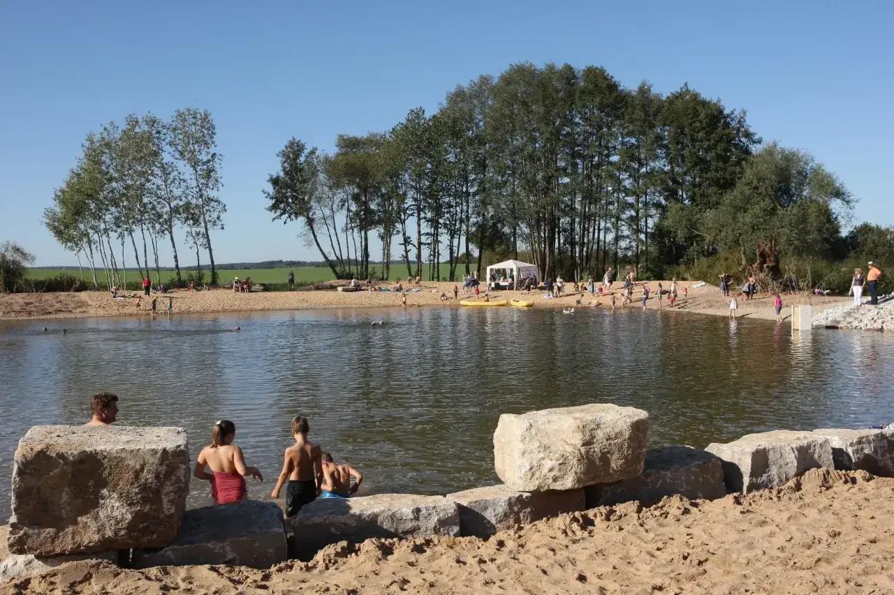 Sonniger Tag am badesee bamberg. Menschen planschen im Wasser, sonnen sich am Sandstrand und genie&szlig;en die Natur.