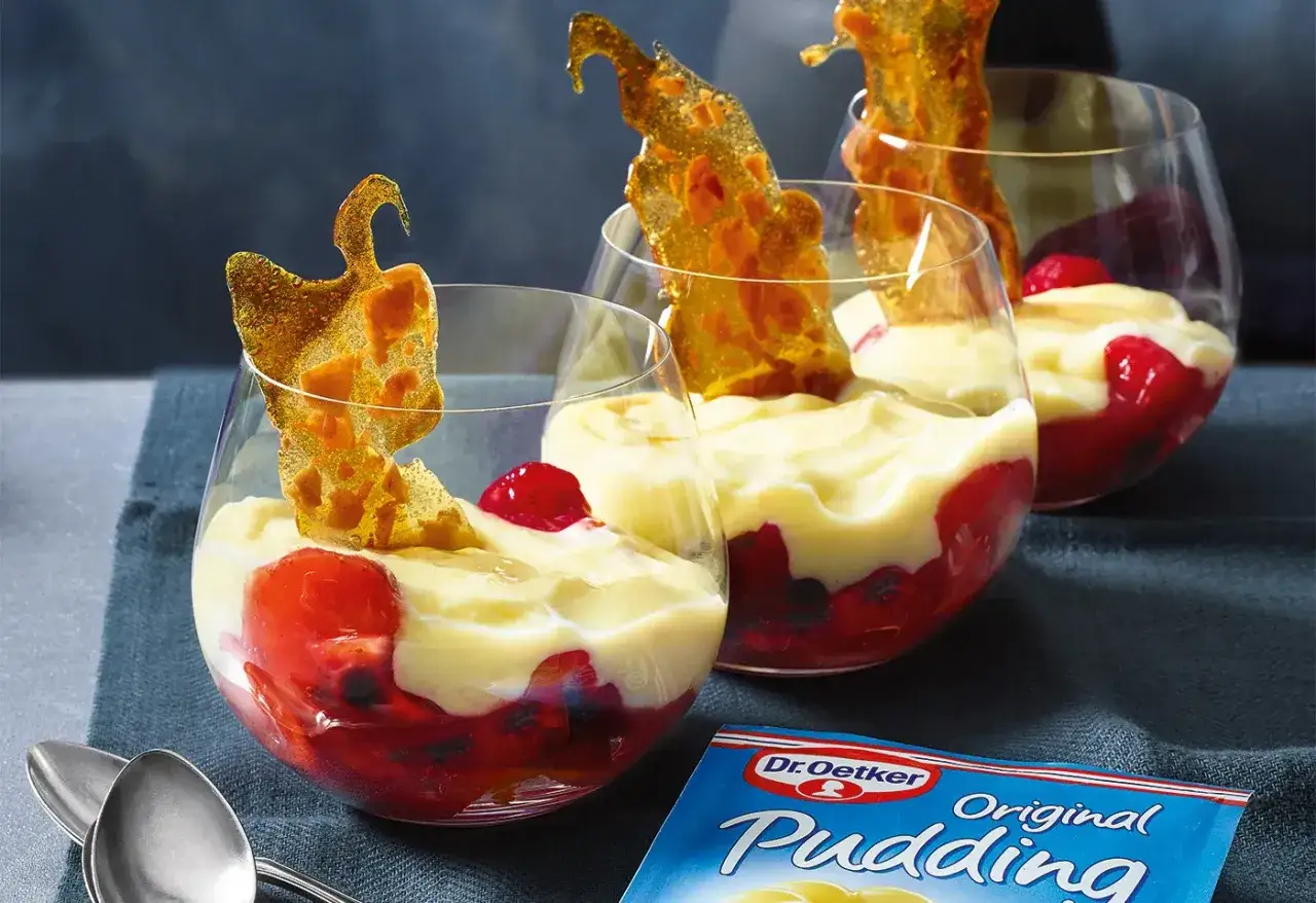 Cremiger Vanille Pudding mit roten Früchten und karamellisierten Zucker-Dekorationen in Gläsern.