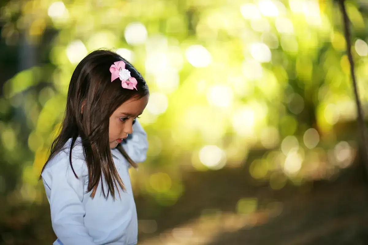 Mała dziewczynka z różową kokardką na głowie, wpatrzona w bok. Piękna bokeh fotografia.