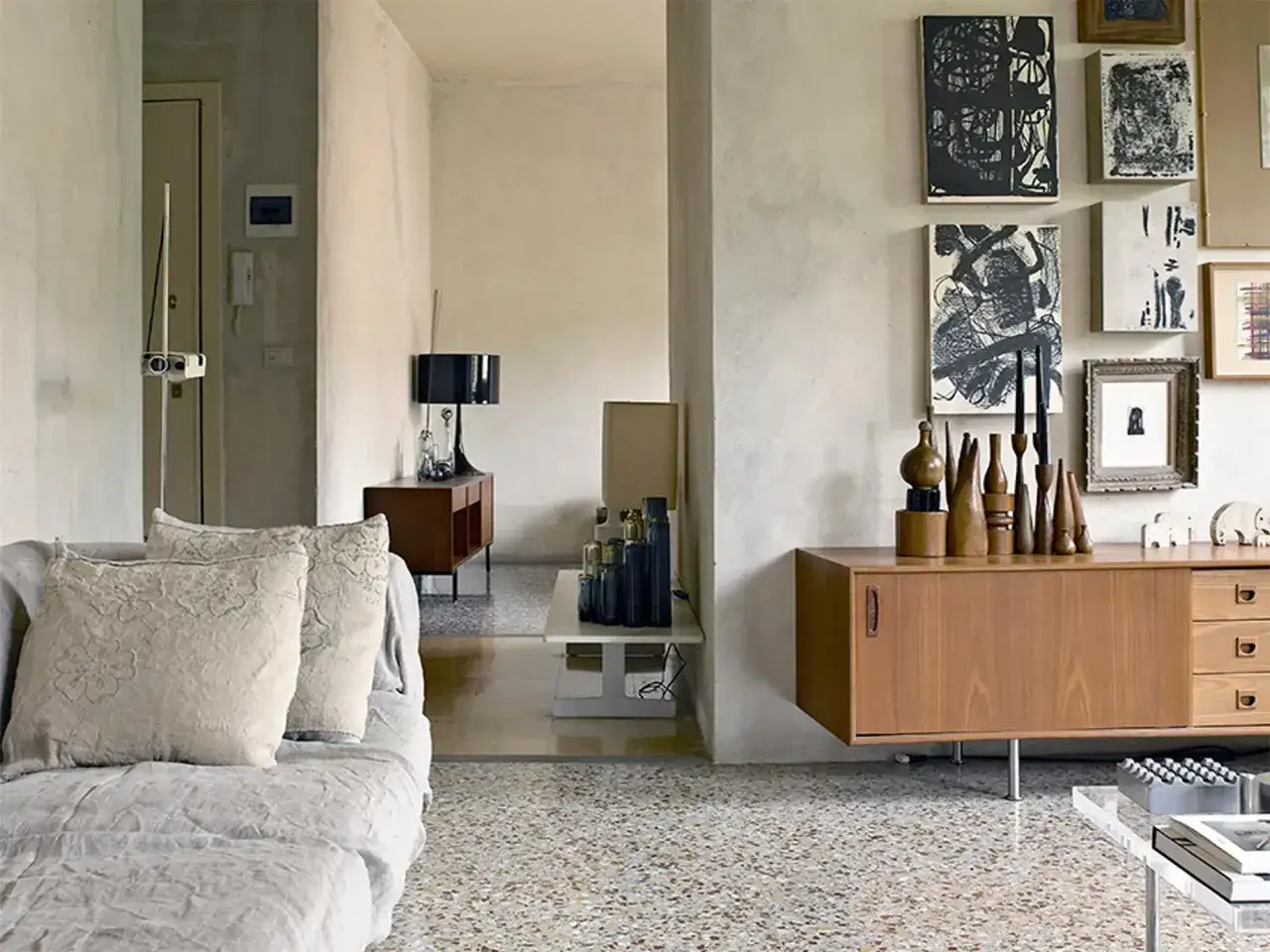Soggiorno con divano grigio, quadri astratti e credenza in legno su pavimenti marmo anni 70.