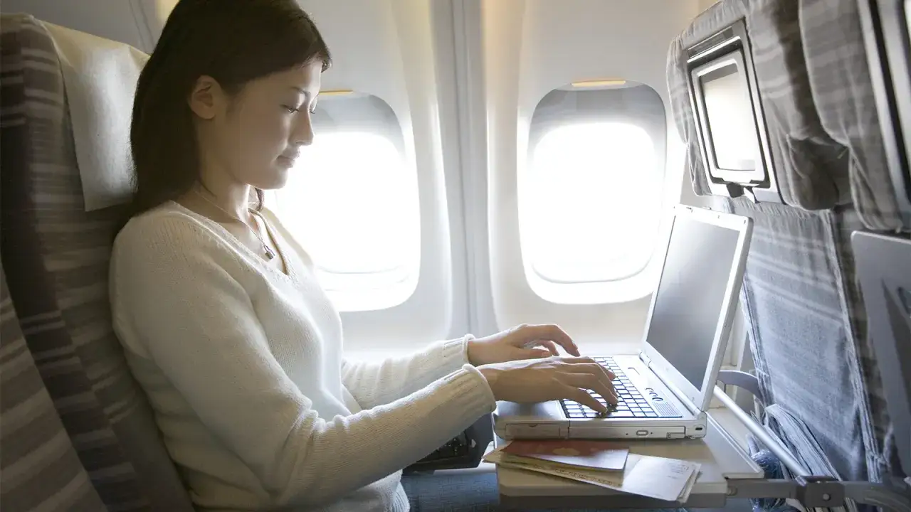 Kobieta pracuje na laptopie w samolocie. Czy w samolocie jest wifi? Z pewnością można się połączyć, by nadrobić zaległości w pracy.