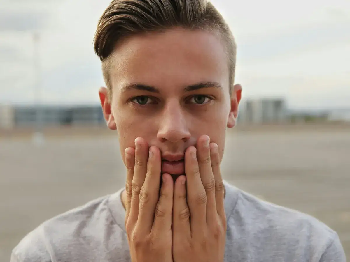 Joven con un corte de pelo taper fade, con las manos en la cara, mirando a la cámara.