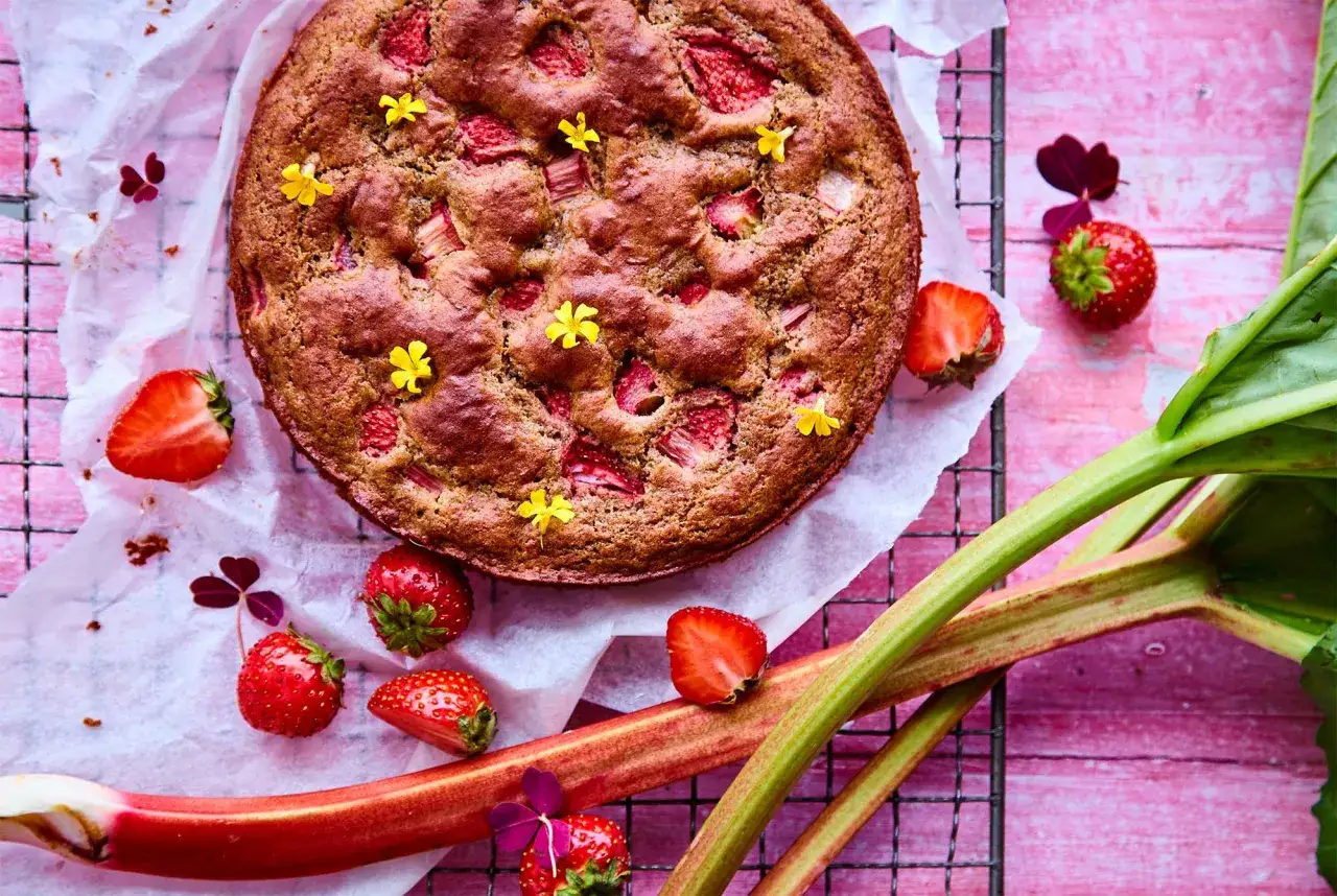 En saftig rabarberkompott tårta med färska jordgubbar och små gula blommor. Perfekt för fikat!