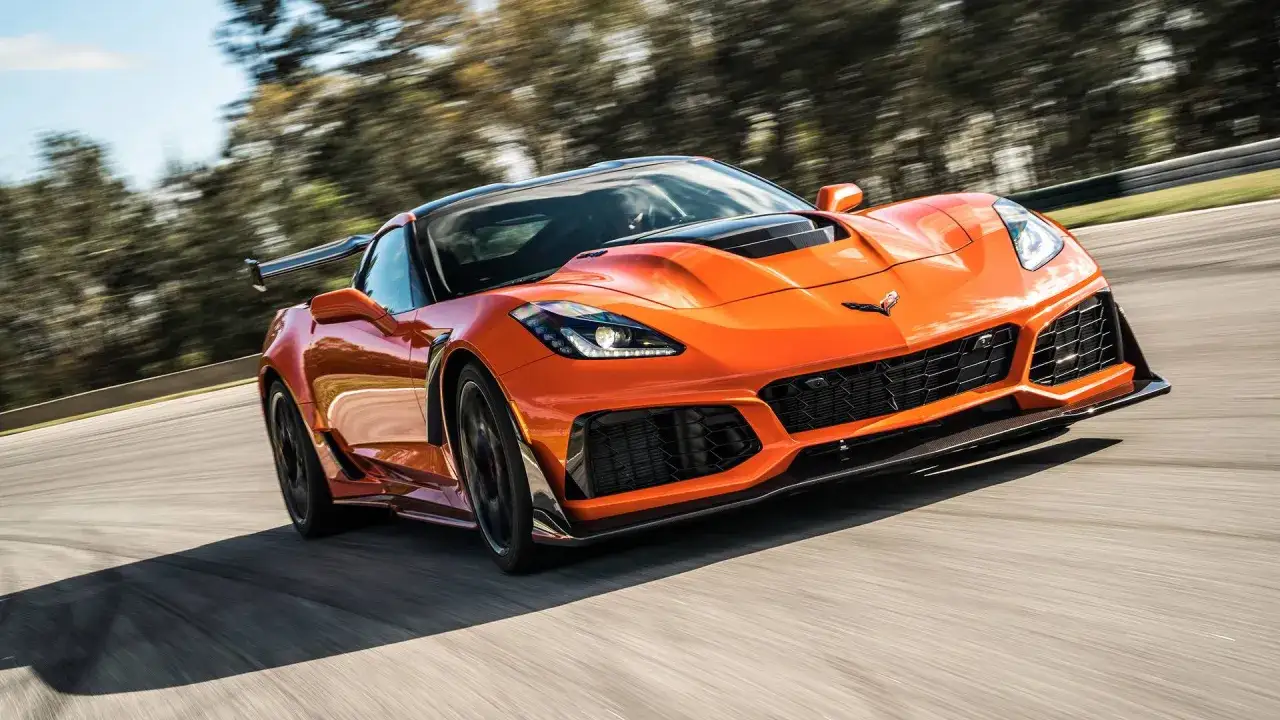 Pomarańczowy **Corvette C7 ZR1** pędzi po torze wyścigowym, jego sylwetka jest dynamiczna, a spojler podkreśla sportowy charakter.