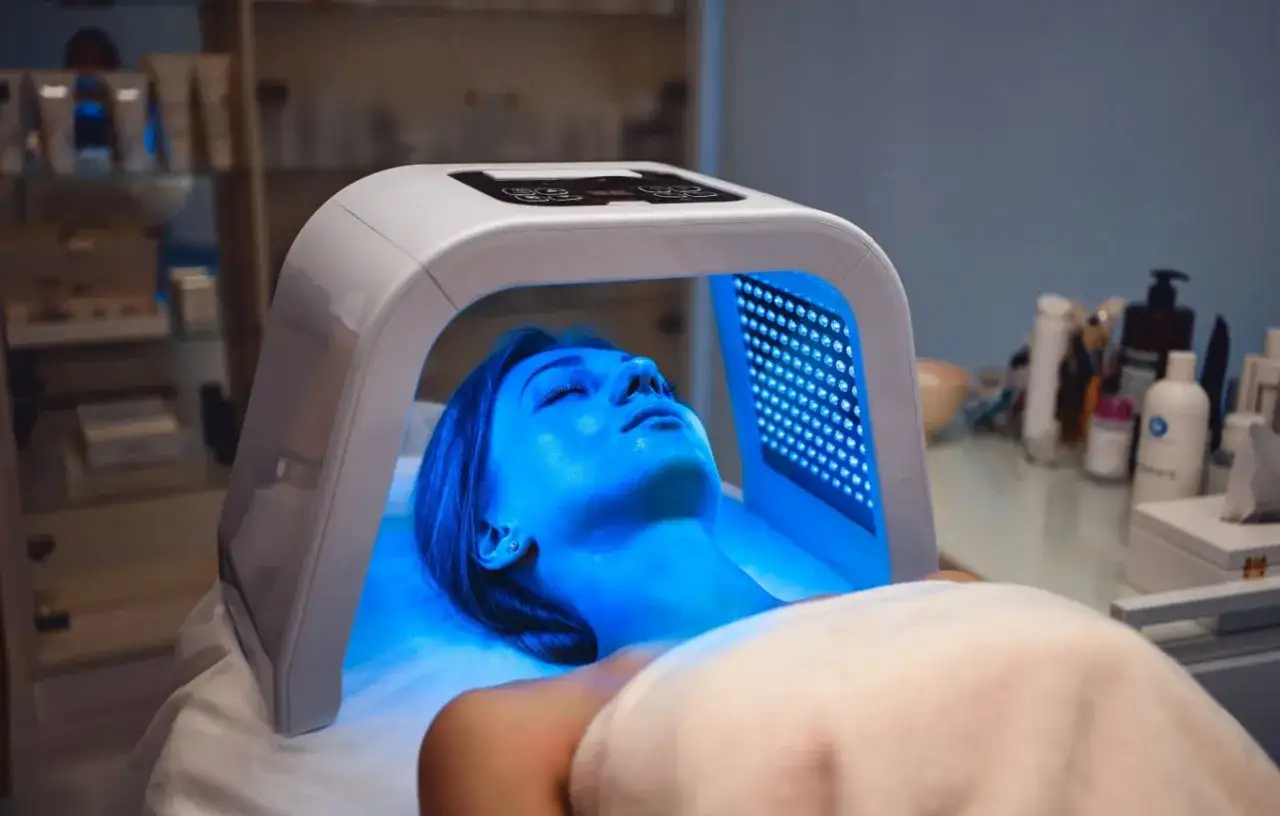 Une femme reçoit un traitement de luminothérapie visage bienfaits. La lumière bleue illumine son visage, promettant une peau éclatante.
