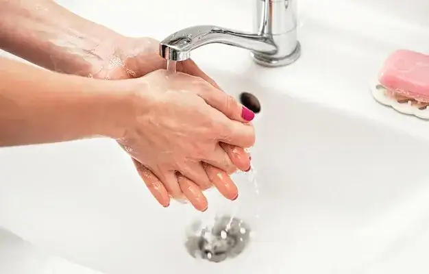 Osoba myjąca ręce pod kranem z mydłem