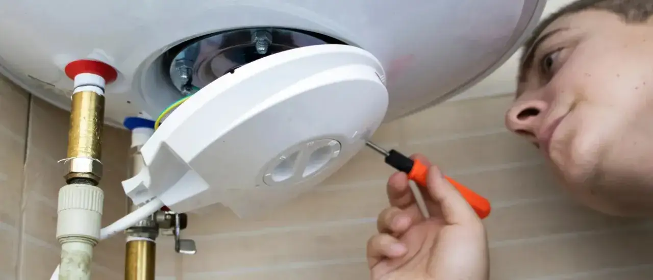 Un jeune homme effectue l'entretien d'un chauffe-eau, serrant une vis avec un tournevis.