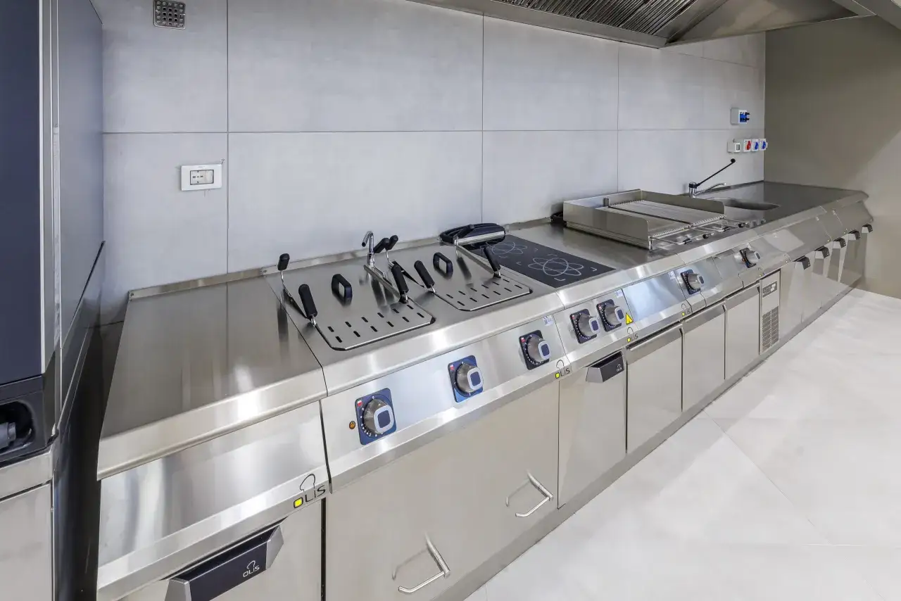 Cucina professionale in acciaio inox, parte di un progetto mensa aziendale. Friggitrici, piastra e piano cottura a induzione.