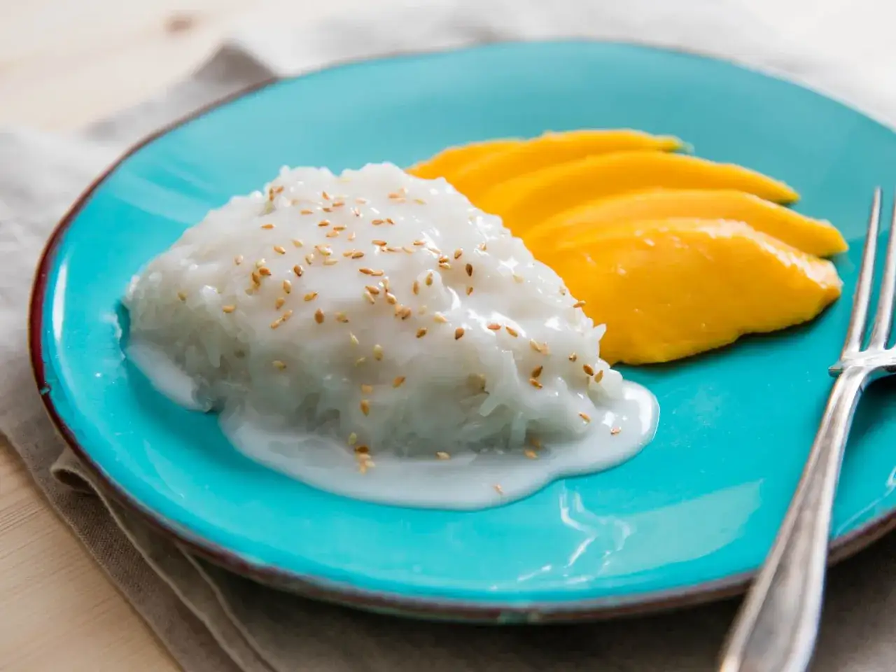Słodki ryż z mlekiem kokosowym i sezamem, podany z plasterkami mango na turkusowym talerzu. Pyszny deser ryż na słodko.