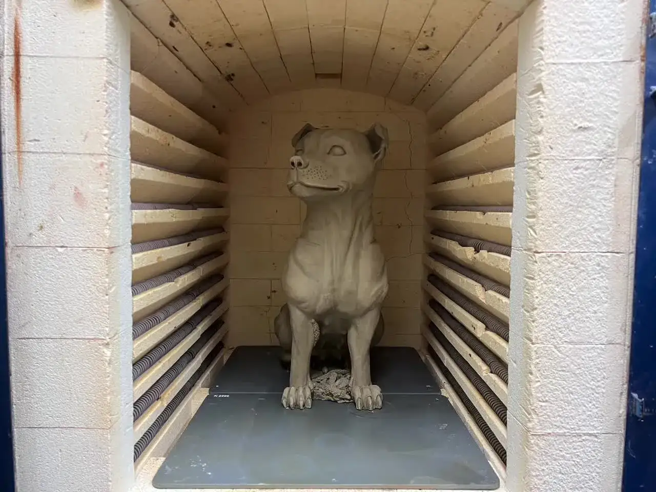 En hundskulptur i blålera keramik väntar på att brännas i en ugn.