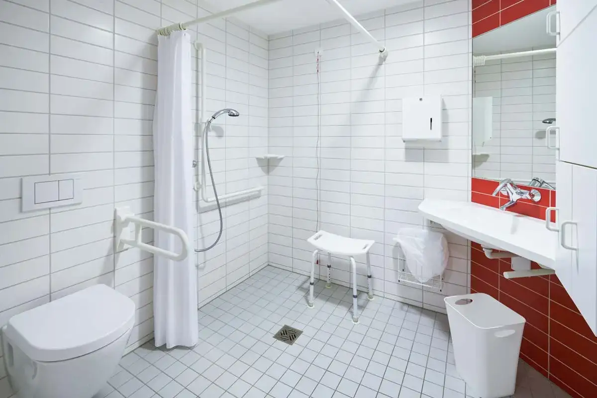 Barrierefreies Bad mit Duschhilfen f&uuml;r Senioren: Toilette mit Haltegriff, Duschhocker, Waschbecken und Spiegel.