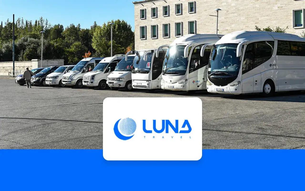Rząd białych busów i autokarów czeka na pasażerów na parkingu. To transport z lotniska Tirana, gotowy na podróż z Luna Travel.