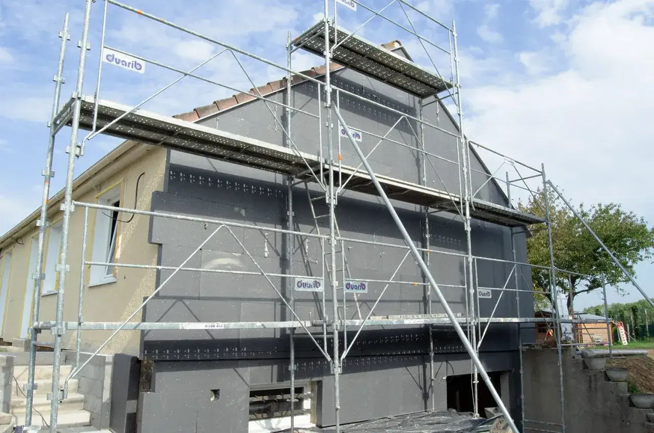 Échafaudage autour d'une maison en cours d'isolation avec 10 matériaux isolants gris.
