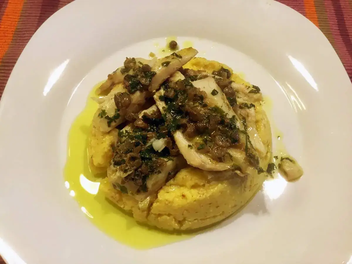 Piatto di luccio in umido su polenta, condito con erbe aromatiche e capperi. Un classico della ricetta luccio in umido.