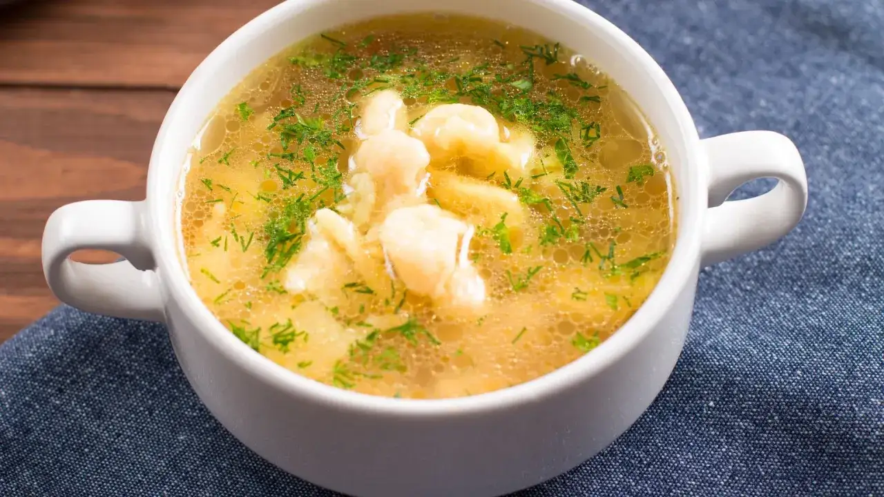 Aromaticzna zupa zacierkowa z zielonym koperkiem w białej miseczce, podana na granatowym obrusie.