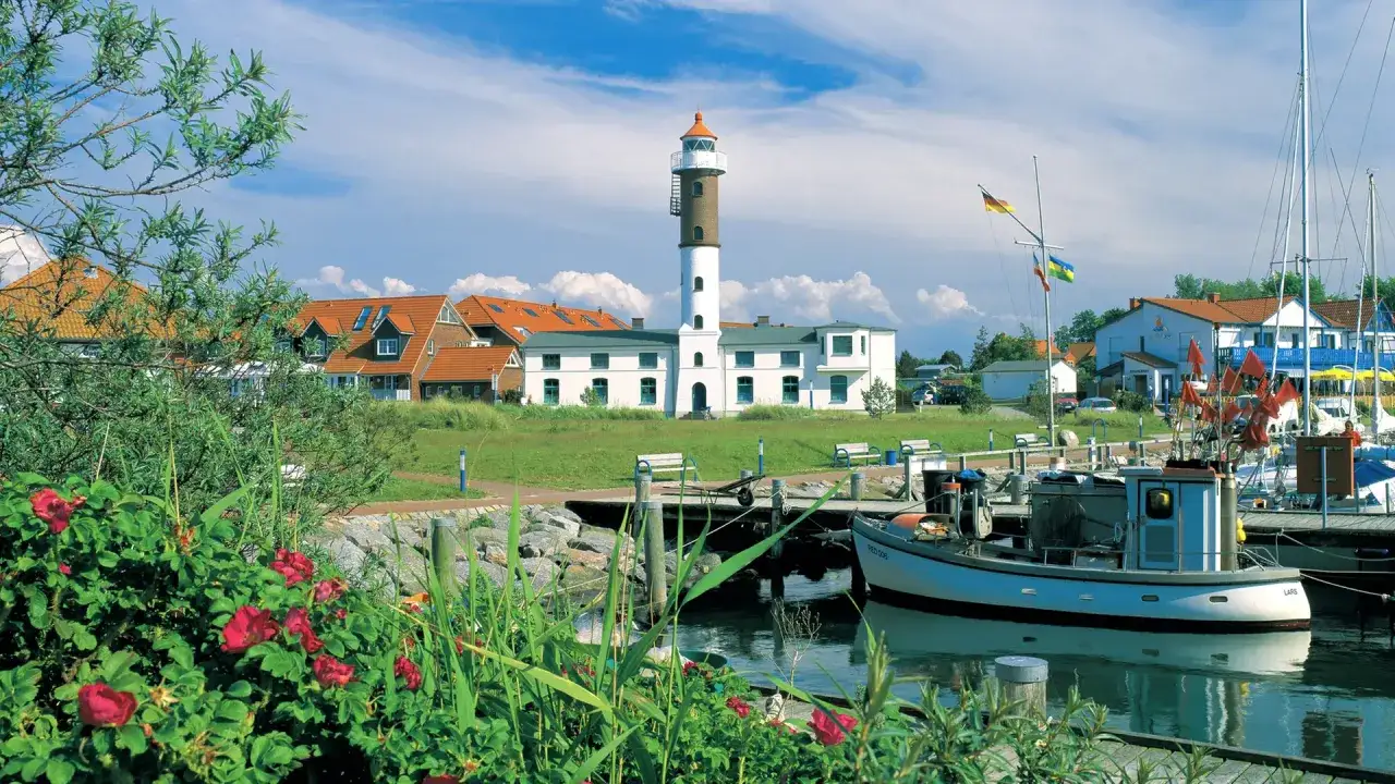 Idyllischer Hafen mit Leuchtturm auf Insel Poel, ein echter Geheimtipp. Boote liegen im Wasser, rote Rosen blühen.