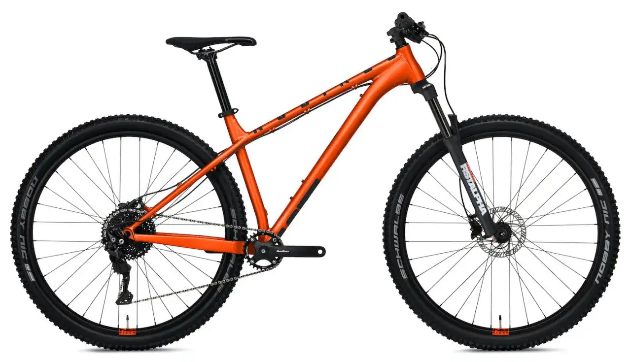 Pomarańczowy rower górski z amortyzatorem z przodu. Czy to hardtail czy full? Ten model to hardtail, idealny na podjazdy i zjazdy.