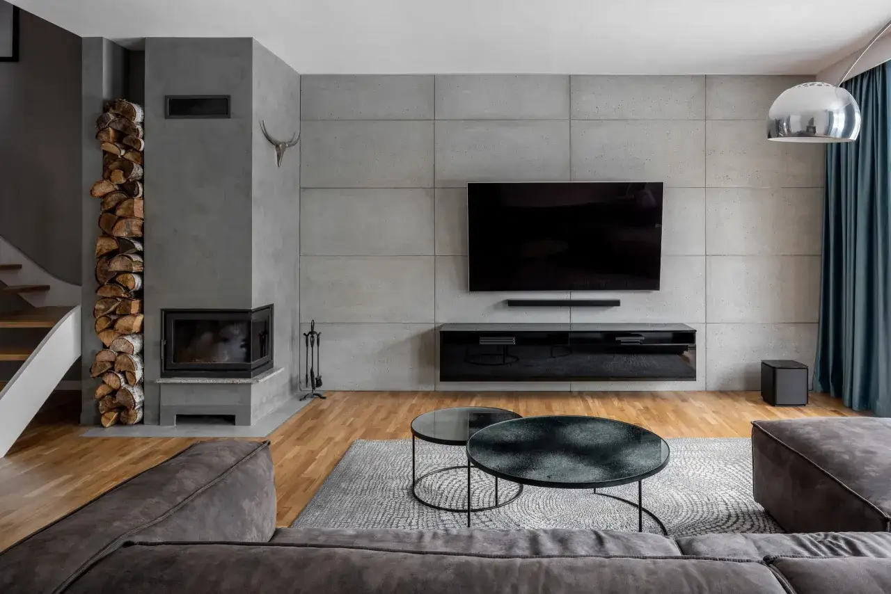 Nowoczesny salon z betonową ścianą, kominkiem i drewnem. Zastanawiasz się, z czym łączyć lamele? Tutaj beton i drewno tworzą stylowe połączenie.