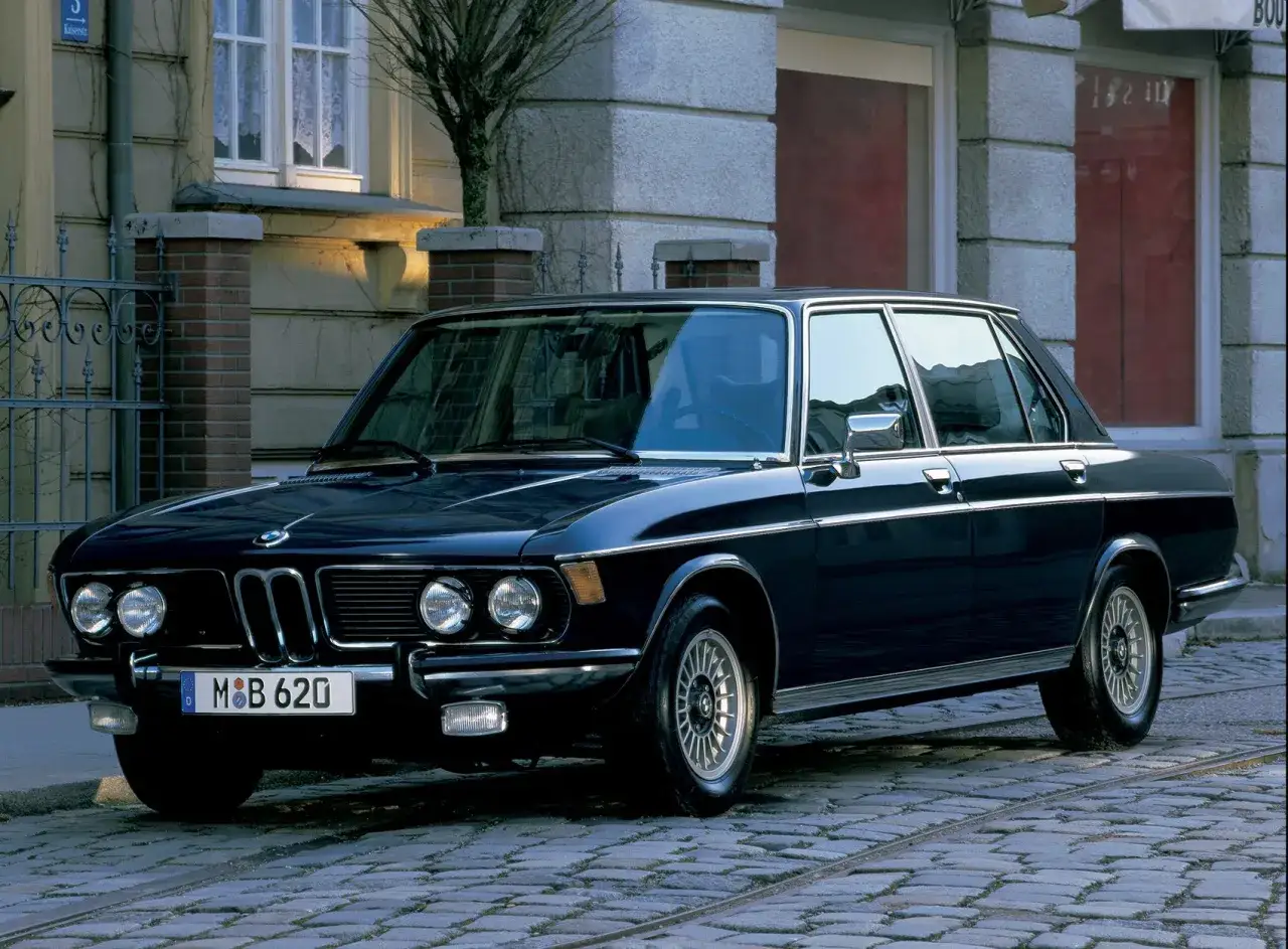 Elegancki, ciemny sedan BMW E50 z lat 70. stoi na brukowanej ulicy przed kamienicą.