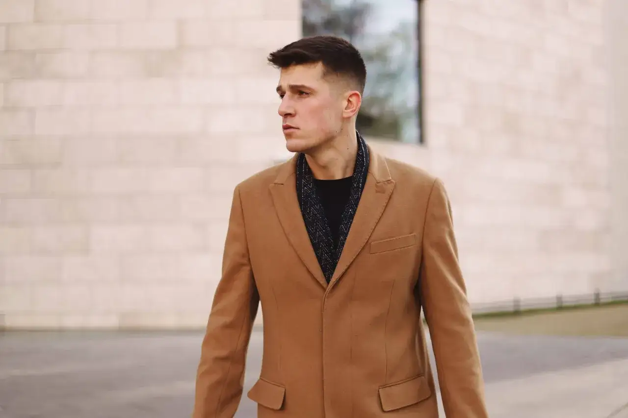 Mężczyzna w płaszczu w kolorze camel, który pasuje do wielu typów urody, prezentuje elegancki styl.