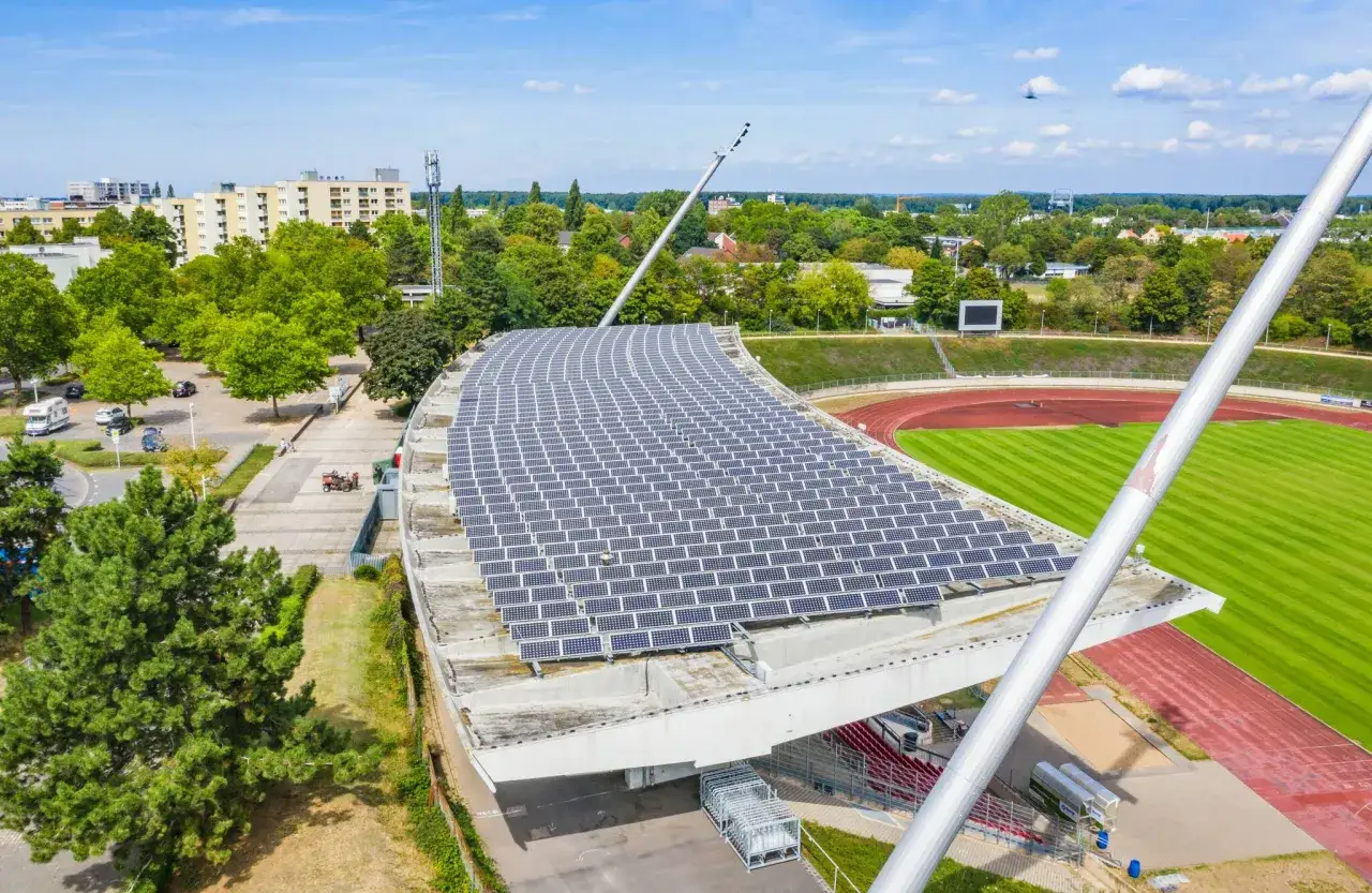 Dach eines Stadions mit Solarmodulen, ein Schritt in Richtung klimaneutral 2035. Daneben eine Laufbahn und grüne Wiesen.