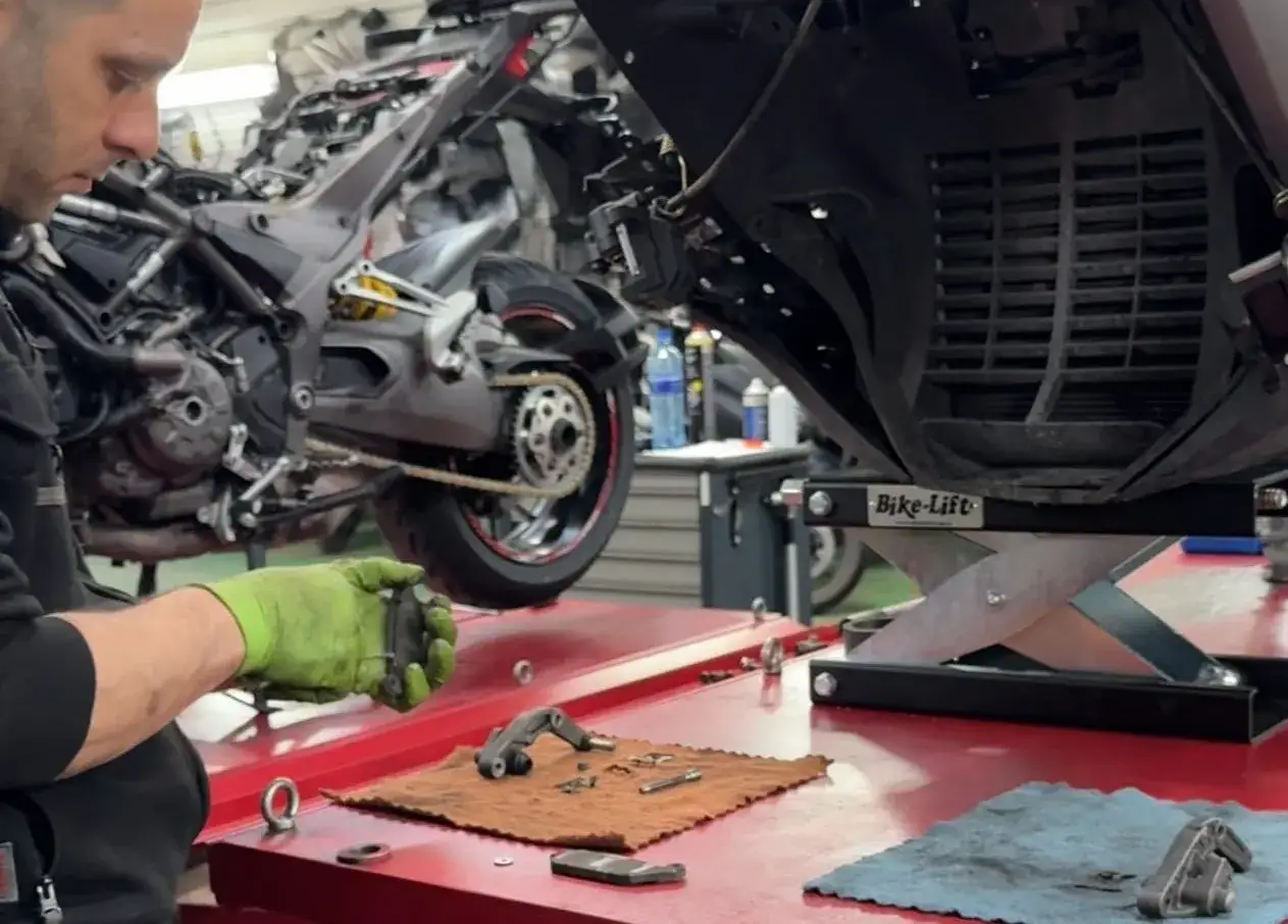 Mec&aacute;nico con guantes verdes realiza el cambio de pastillas de freno de una moto en taller.