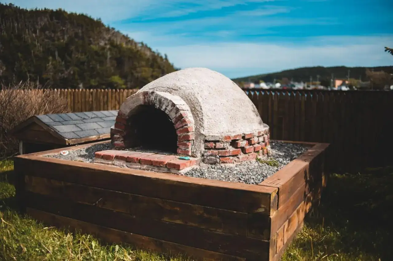 En hemmagjord pizzaugn i tegel och cement, byggd enligt en ritning. Den står i en träram utomhus.