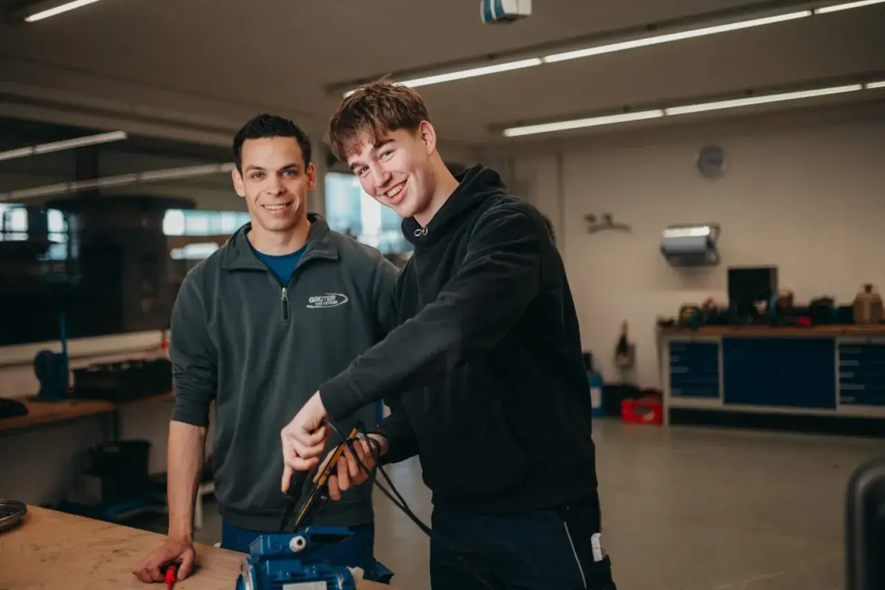 Zwei junge M&auml;nner in einer Werkstatt, die an einem Ger&auml;t arbeiten. Eine einfache Ausbildung kann zu viel Geld f&uuml;hren.