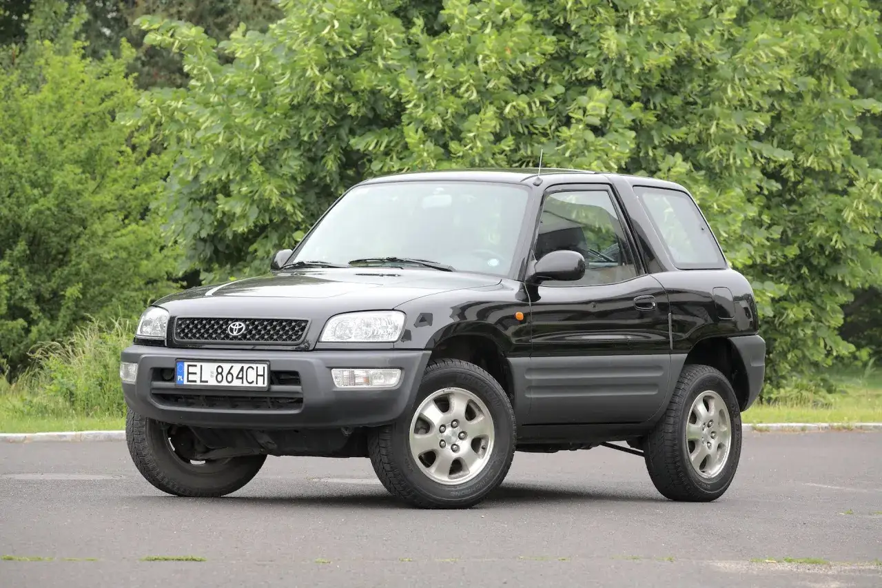 Czarny, trzydrzwiowy SUV Toyota RAV4, jeden z niezniszczalnych aut do 10 tys. zł, zaparkowany na tle zieleni.