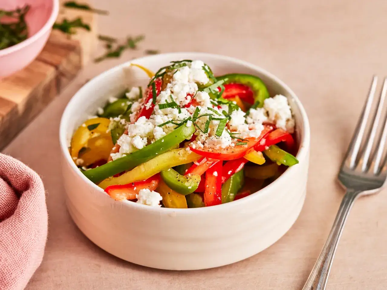 Bunter Paprika Salat mit Feta-Käse und Kräutern in einer Schüssel, daneben eine Gabel und eine Serviette.