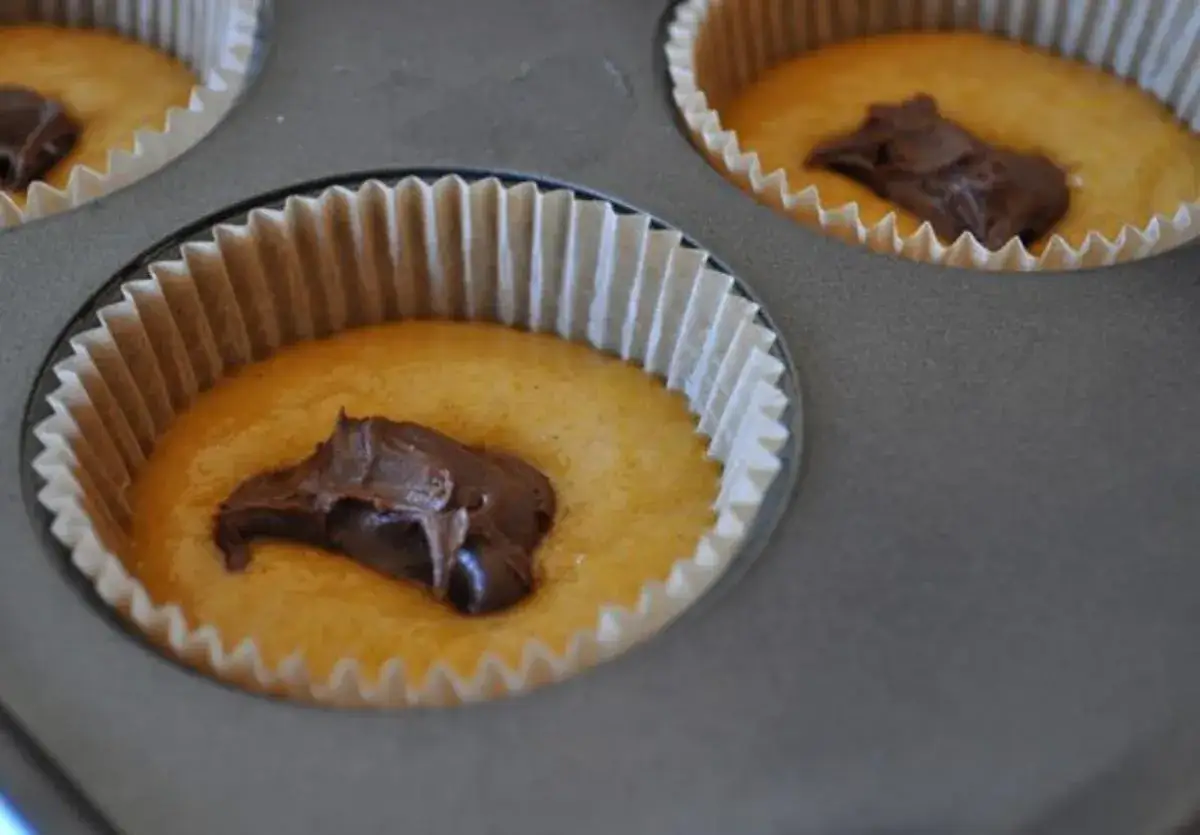 Zwei Muffinformen mit Teig, in denen jeweils ein Klecks Nutella liegt. Bald gibt es leckere Nutella Muffins!