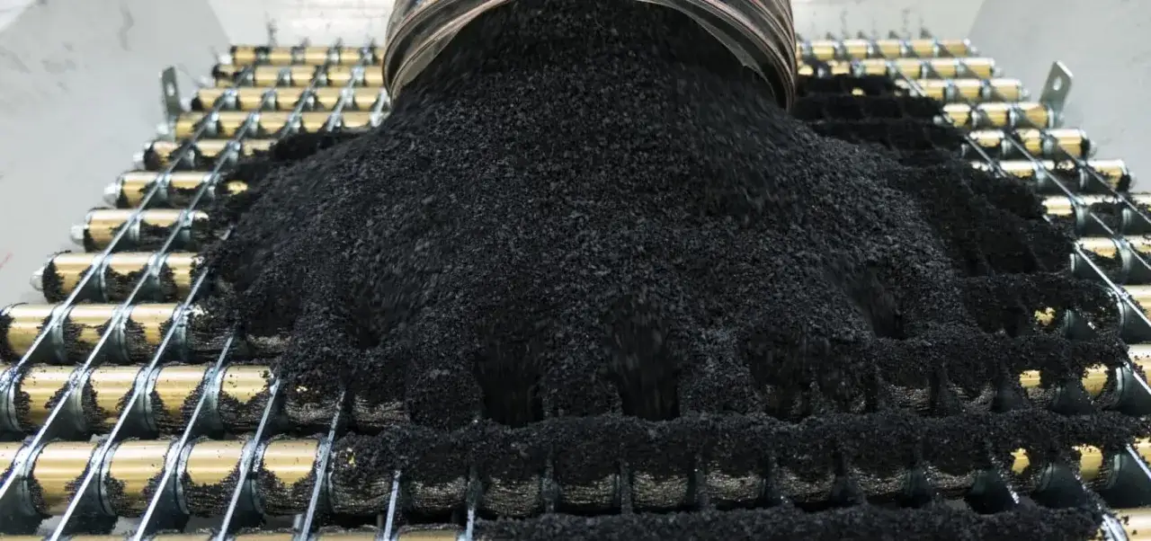 Granulat z recyklingu opon opłacalność procesu. Czarna, drobna masa spada na metalowe rolki.